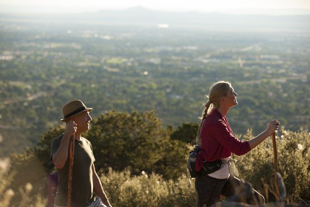 Two hikers walk along an outcropping above Santa Fe, with the city receding into the distance.